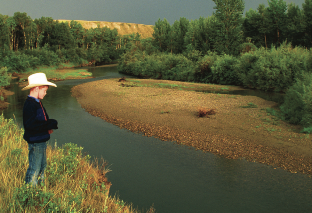 Young boy wearing a cowboy hat looking at a river in a riparian area